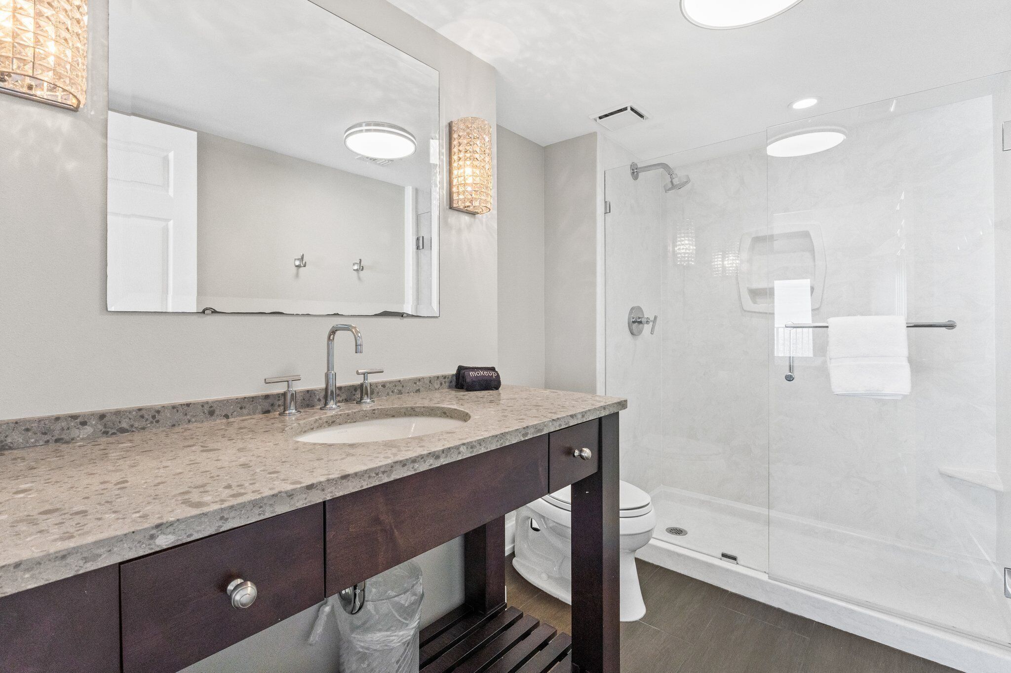 A modern bathroom with a granite countertop sink, a large mirror, a shower enclosure, and a toilet.