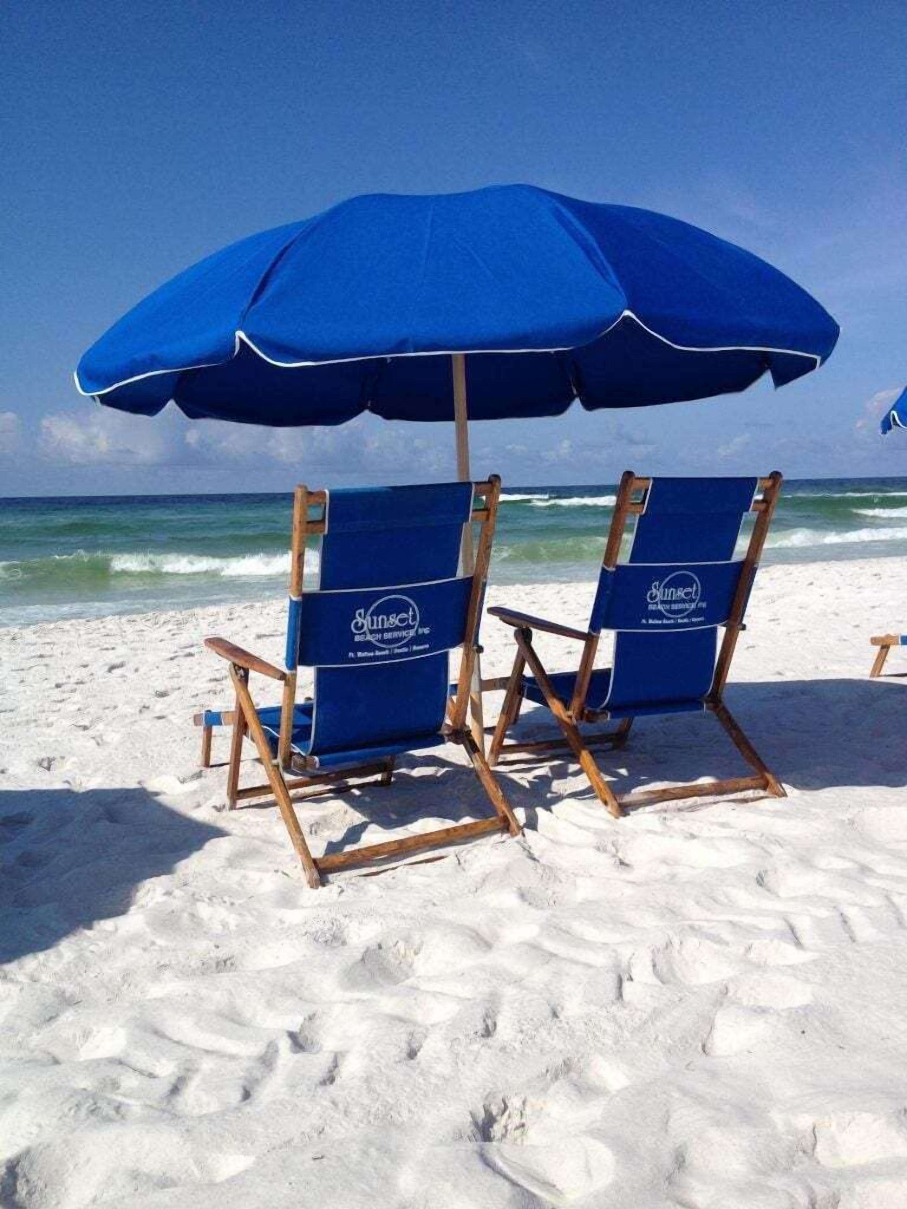 Twee strandstoelen met een blauwe parasol op een zandstrand.