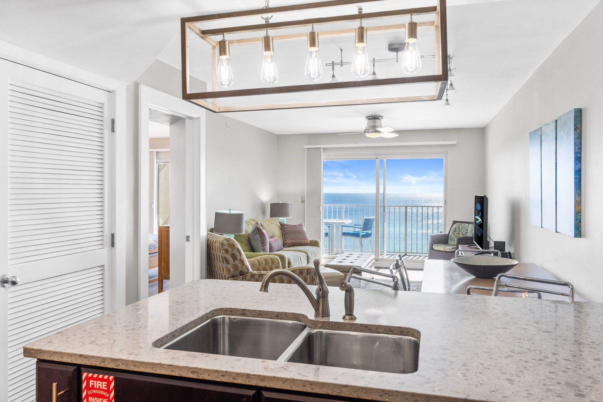 A modern kitchen with a double sink, a dining area with a table and chairs, and a balcony with a view.