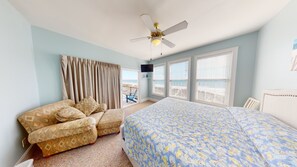 A bedroom with a bed, a chair, a ceiling fan, a TV, and a view of the beach. - Margarita Villas A (North Myrtle Beach)