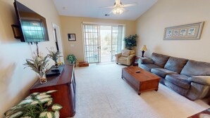 A living room with a sofa, coffee table, TV, and plants. - Ironwood 1233 (North Myrtle Beach)