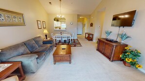 A living room with a sofa, coffee table, TV, and a dining area with chairs and a table. - Ironwood 1233 (North Myrtle Beach)