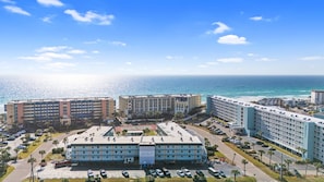A hotel complex with multiple buildings, a parking lot, and a view of the ocean. - Venus 216 - Starfish Cove (Fort Walton Beach)