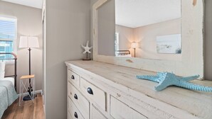 A bedroom with a bed, a dresser, a mirror, a starfish decoration, a lamp, and a window with blinds. - Venus 216 - Starfish Cove (Fort Walton Beach)
