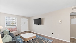 A living room with a sofa, a coffee table, a flat-screen TV mounted on the wall, and a patterned rug. - Venus 216 - Starfish Cove (Fort Walton Beach)