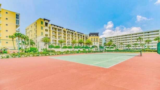 A tennis court surrounded by buildings with balconies and palm trees. - Venus 216 - Starfish Cove (Fort Walton Beach)