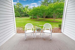 A porch with two white chairs and a small table with a plant, overlooking a well-maintained lawn and trees. - Havens 432 (North Myrtle Beach)