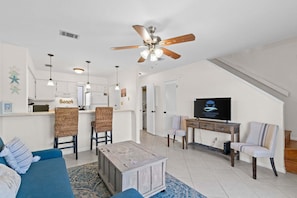 A living room with a blue sofa, a coffee table, and a TV on a wooden stand. - Beach, Please (Fort Walton Beach)