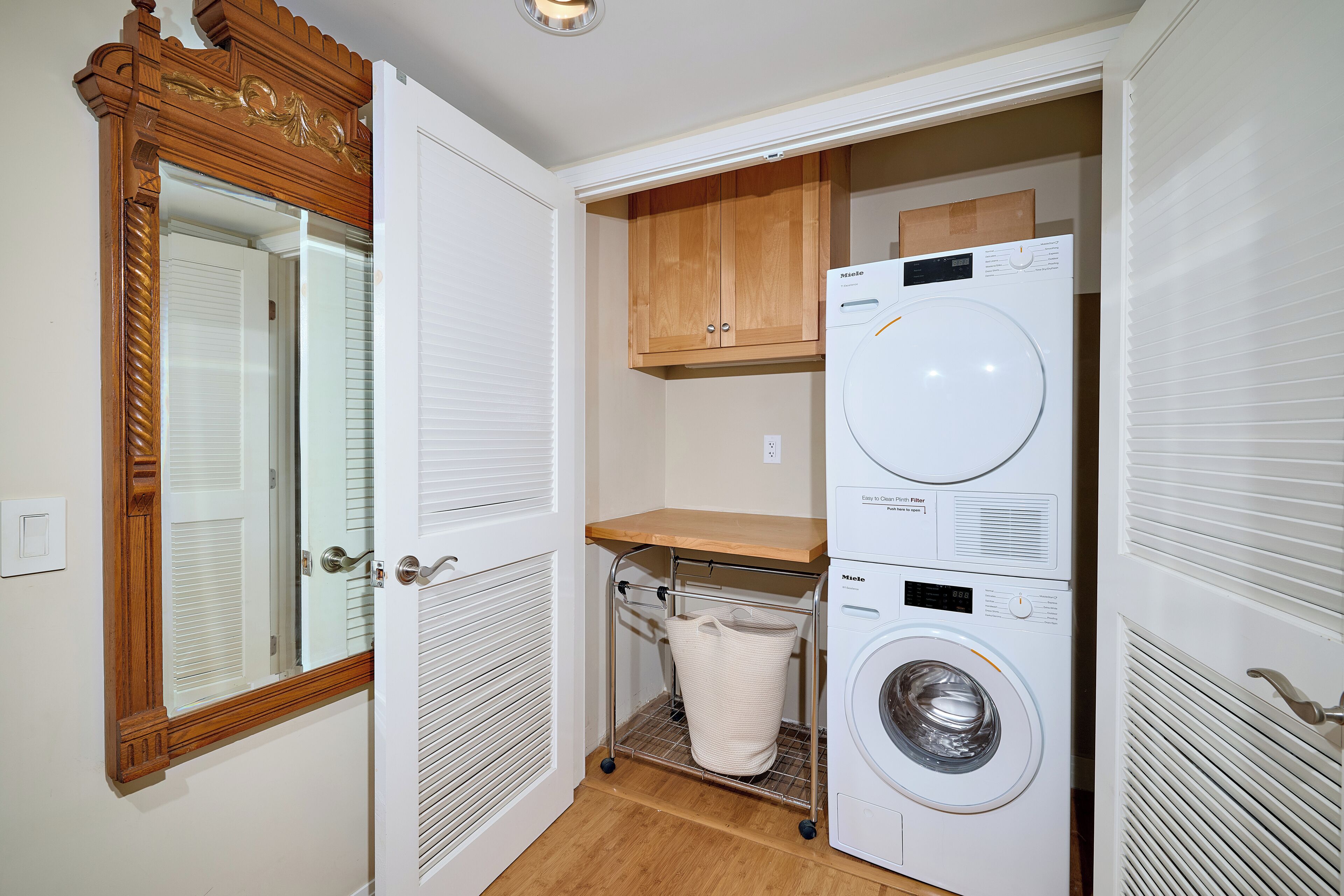 A laundry room with a washing machine, a wooden cabinet, and a metal cart with a laundry basket.