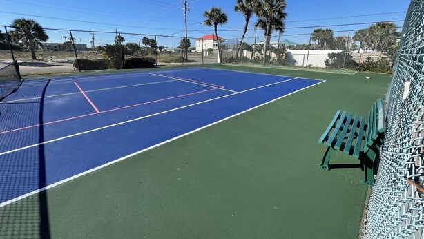 Una cancha de tenis al aire libre con superficie azul y zona verde circundante.