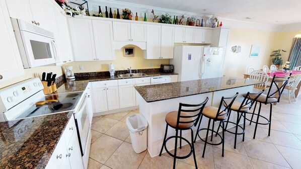 A modern kitchen with white cabinets, granite countertops, a built-in oven, and a central island with bar stools. - Atlantis Villas 205 (North Myrtle Beach)