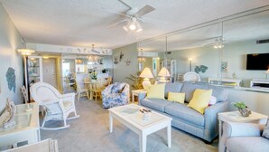 A living room with a sofa, chairs, a coffee table, and a dining area with a chandelier. - 446 El Matador (Fort Walton Beach)