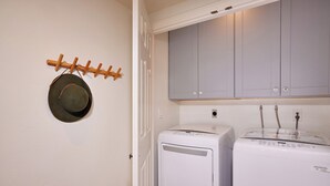 A laundry room with two white washing machines, a drying rack with a hat, and grey cabinets above. - 152-6 S Pacific Fantastic Ocean View (Oceanside)