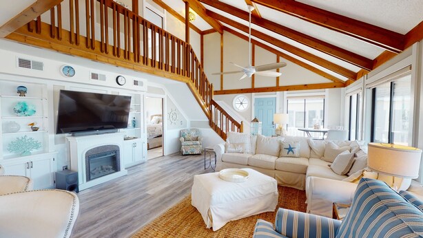 A spacious living room with a fireplace, a large TV, and a staircase leading to an upper level. - Wait & Sea (North Myrtle Beach)