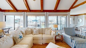 A spacious living room with a large beige sectional sofa, a blue-striped armchair, and a small side table with a lamp. Large windows offer views of the city. - Wait & Sea (North Myrtle Beach)