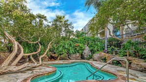 A hot tub surrounded by lush greenery and a stone pool, with a metal ladder for access. - North Coast Village B212 (Oceanside)
