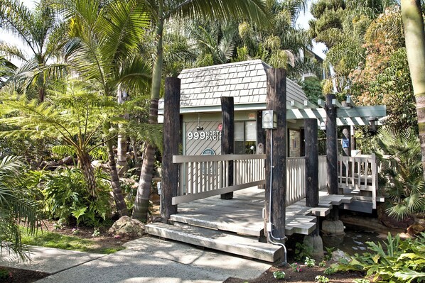 A small, rustic building with a sign reading "999 North Pacific" surrounded by lush greenery and a stone pathway. - North Coast Village B212 (Oceanside)