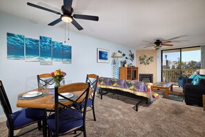 A living room with a dining area, ceiling fans, artwork, and a view through large windows. - North Coast Village B212 (Oceanside)