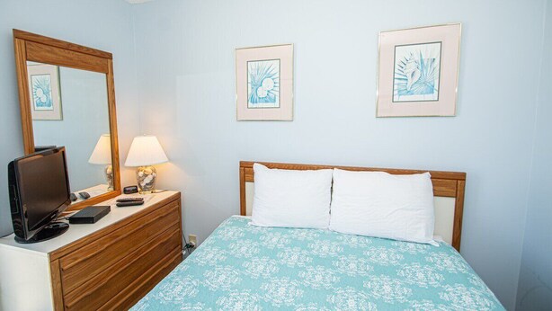 Une chambre à coucher comprenant un lit, une commode, un téléviseur et des œuvres d’art encadrées accrochées au mur.