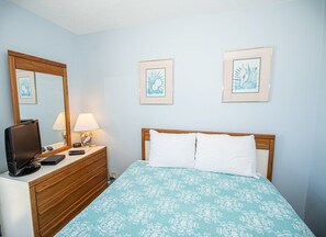 Ein Schlafzimmer mit einem Bett, einem Schminktisch, einem Fernseher und gerahmten Bildern an der Wand.