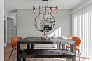 A dining area with a dark wooden table, two orange chairs, a large mirror, and a modern chandelier.