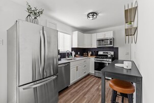 A modern kitchen with stainless steel appliances, white cabinets, a black backsplash, and a wooden floor.