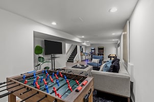 A modern living room with a foosball table, a sofa, a television, and a staircase leading to another level.