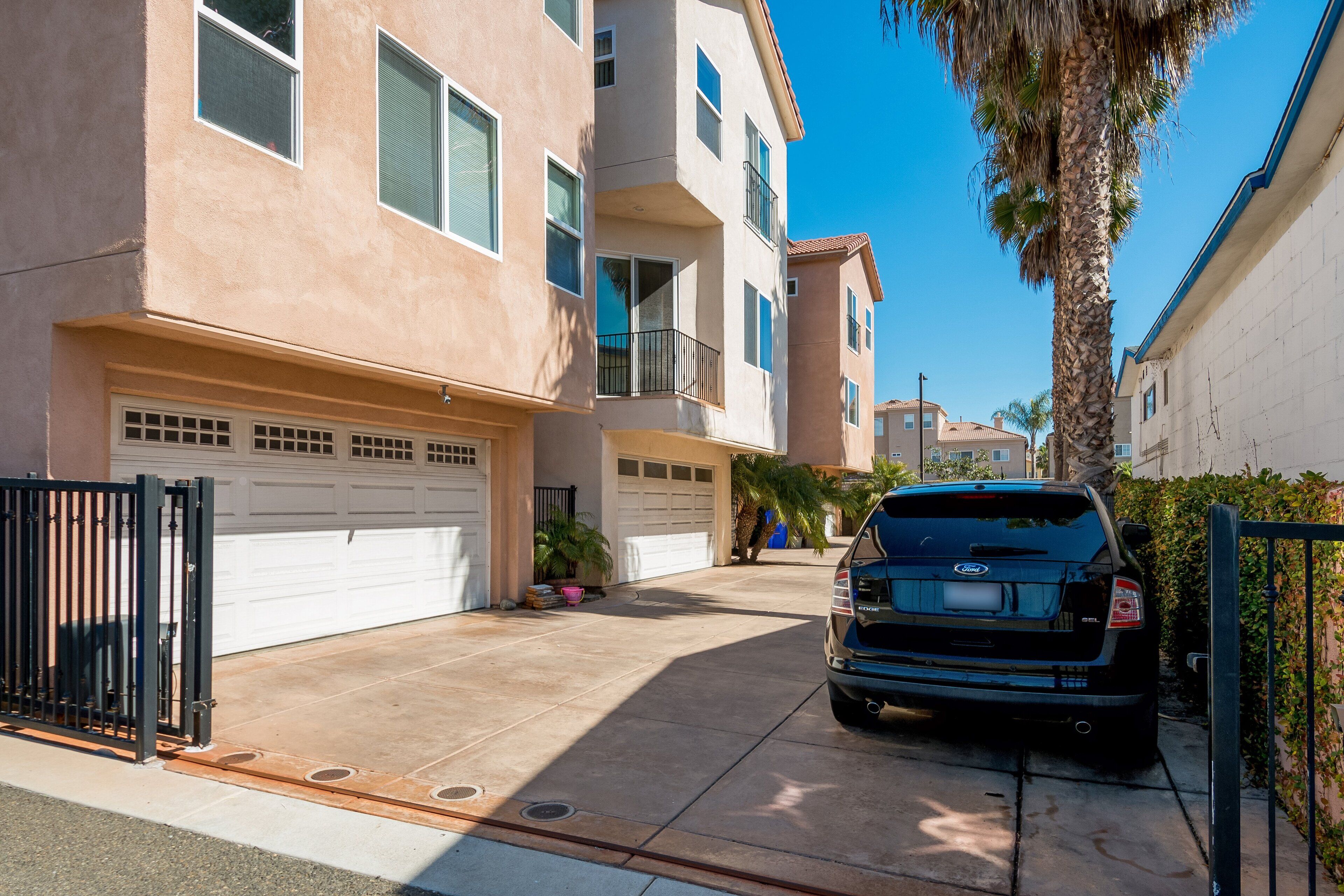 A residential building with a garage, a parked SUV, and a palm tree.