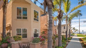 A two-story building with a beige exterior, multiple windows, and a well-maintained garden with various plants and a pathway. - Oceanview Beach Home - 209w (Oceanside)