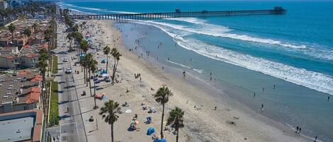 A beach with a long pier extending into the ocean, palm trees lining the shore, and people enjoying the beach.