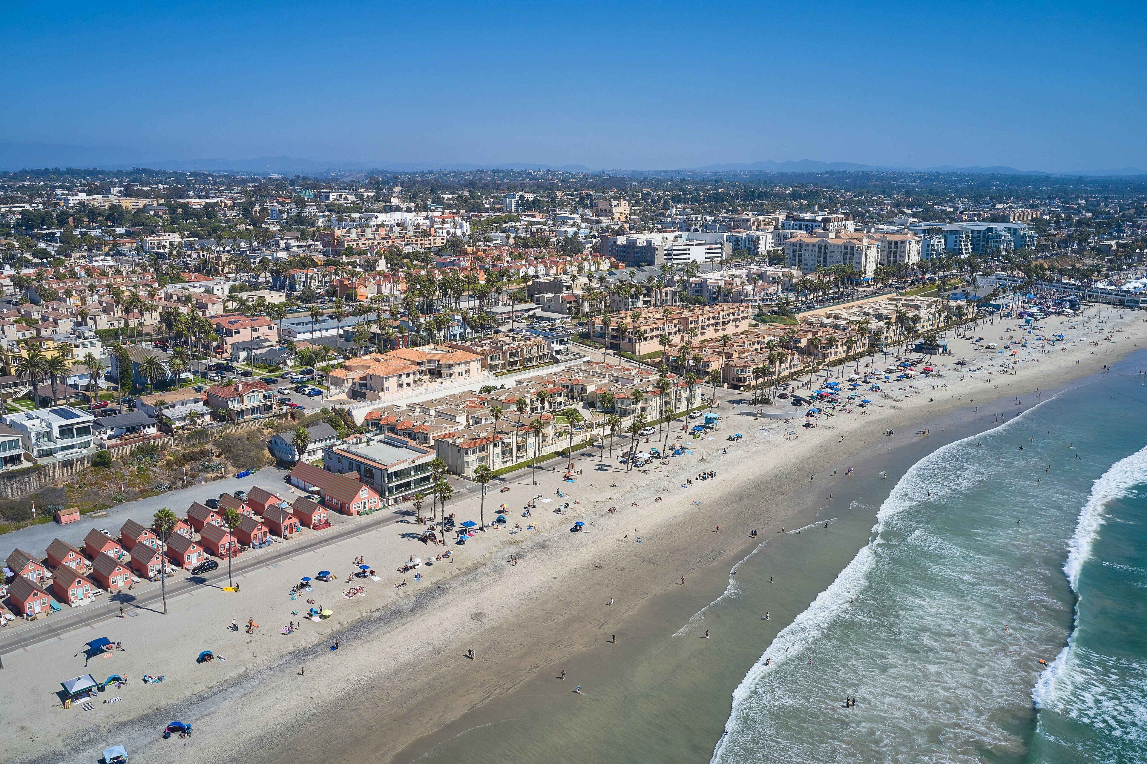 An aerial view of a coastal city with a wide beach, numerous buildings, and a clear sky.