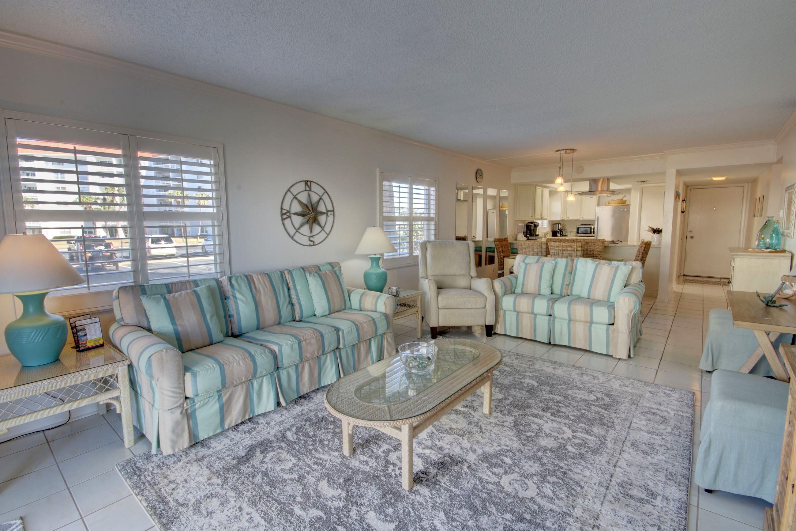 A living room with striped sofas, a coffee table, and a view of the street through large windows.
