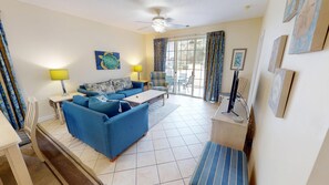 A living room with a sofa, a coffee table, a TV, and a ceiling fan. - Ironwood 1311 (North Myrtle Beach)