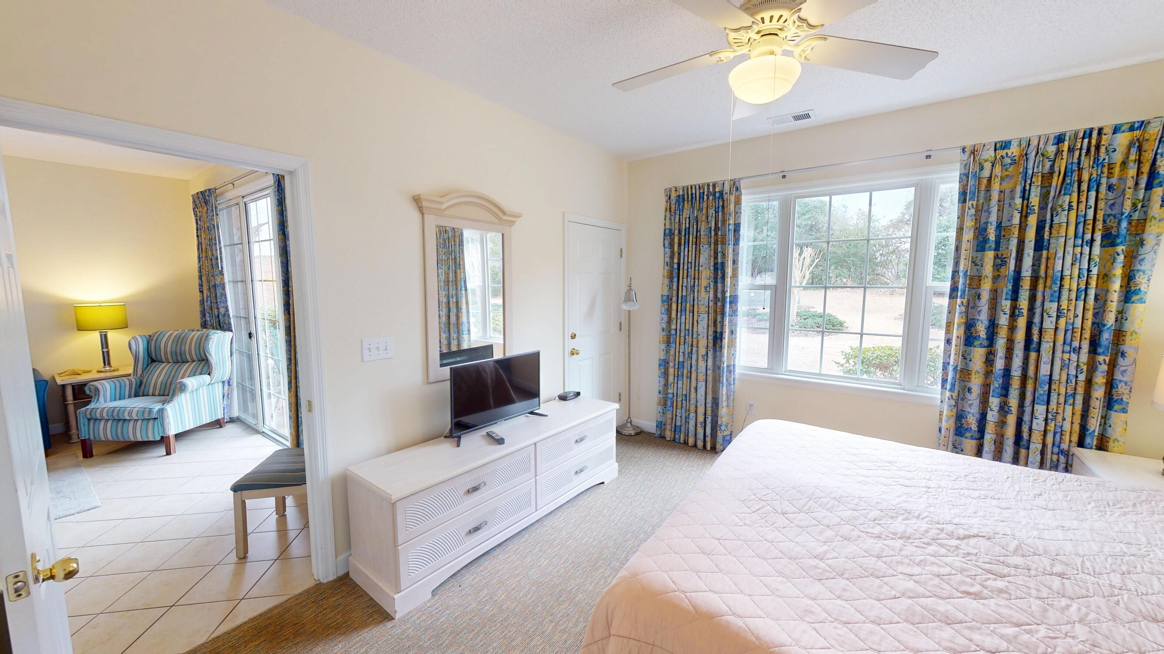 A hotel room with a bed, a TV, a dresser, a chair, and a window with curtains.