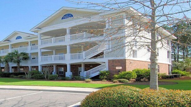 A multi-story hotel with balconies, a covered entrance, and a parking lot. - Arbor Trace 311 (North Myrtle Beach)