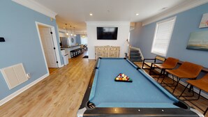 Une table de billard avec des billes, un téléviseur et un coin salon avec des chaises.