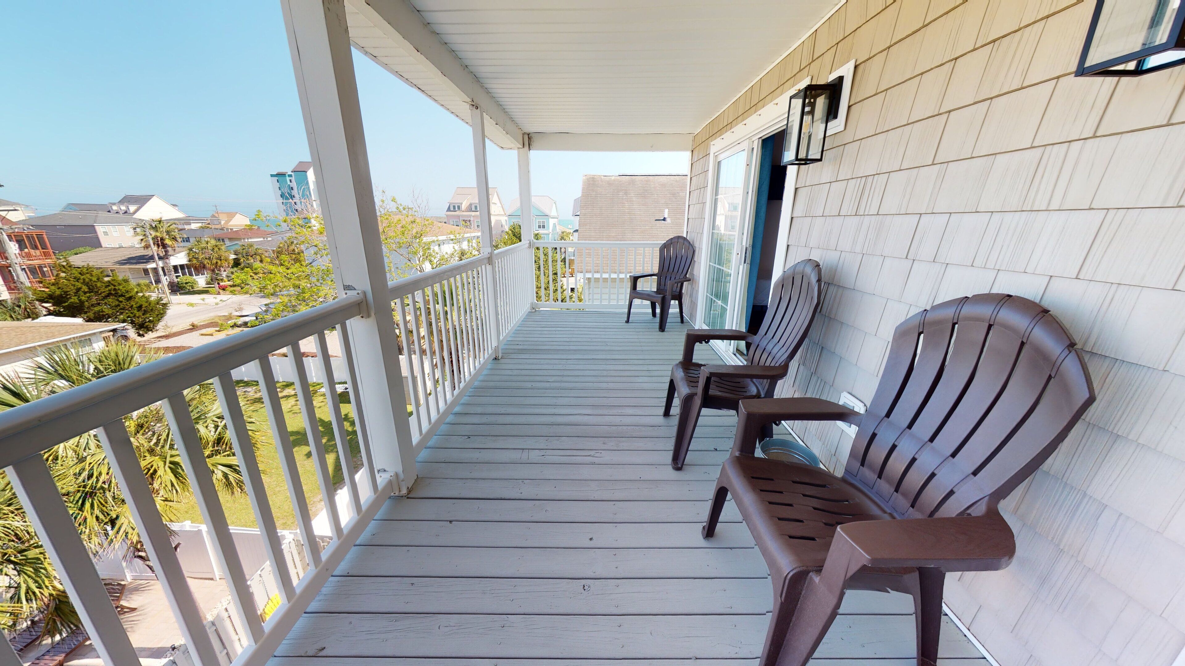 A wooden porch with white railings, two Adirondack chairs, and a view of the neighborhood.