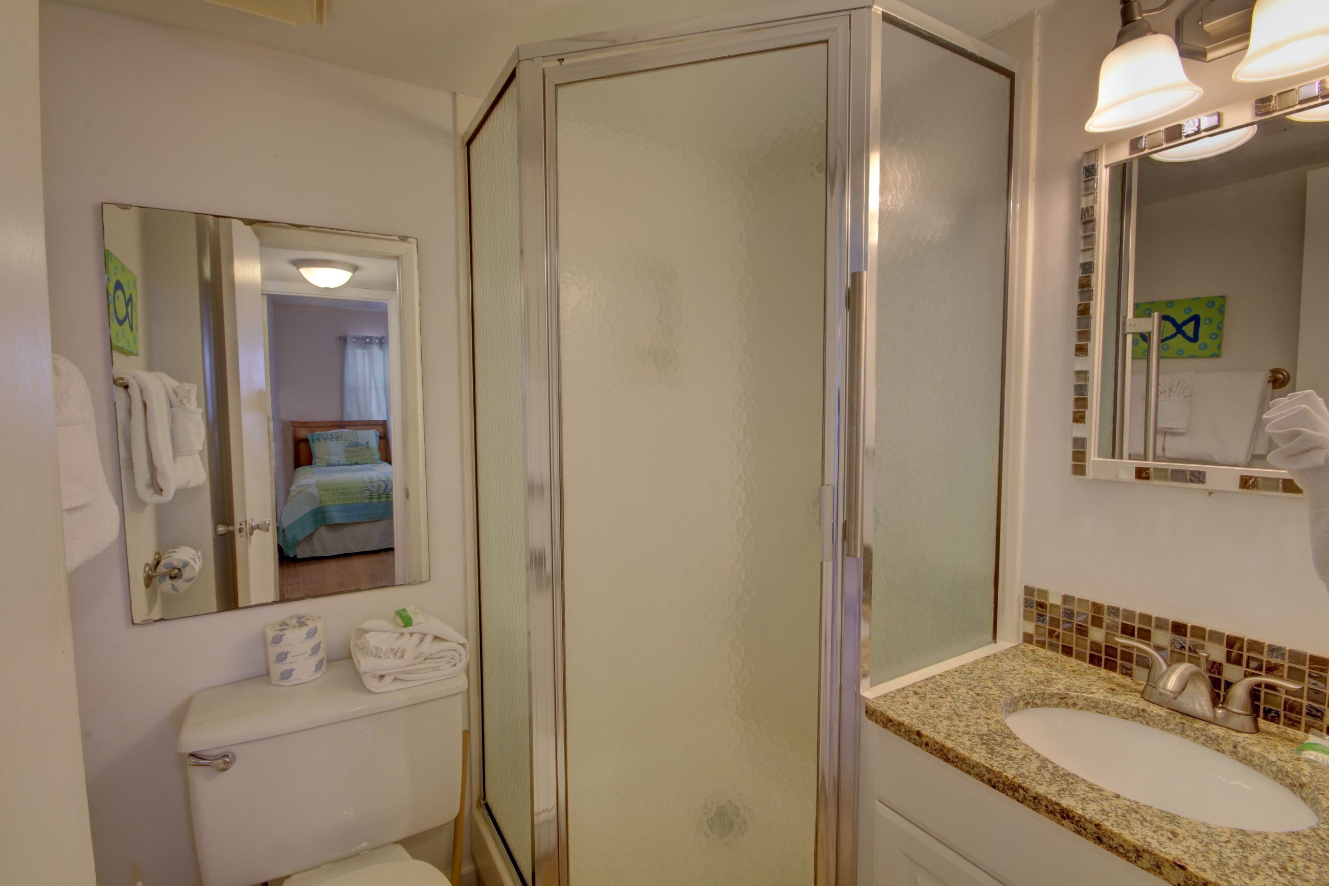 A bathroom with a toilet, a sink, a mirror, and a shower enclosure.