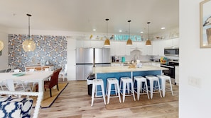 A modern kitchen with white cabinets, stainless steel appliances, and a blue island with bar stools. - Bermuda Breeze - A (North Myrtle Beach)