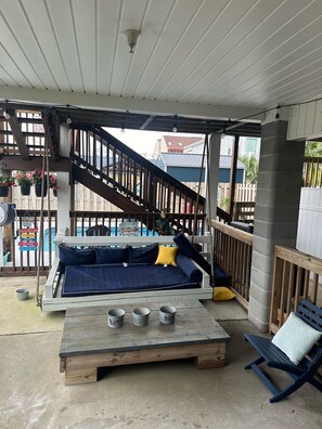A covered outdoor seating area with a wooden bench, a small table with metal cups, and a wooden staircase. - Bermuda Breeze - A (North Myrtle Beach)