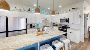 A modern kitchen with white cabinetry, a marble island, stainless steel appliances, and decorative bird figures. - Bermuda Breeze - A (North Myrtle Beach)