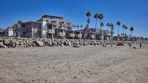 A beach with a rocky shoreline, palm trees, and multi-story buildings in the background. - North Coast Village Cottage G20 (Oceanside)