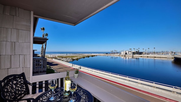 A balcony with a view of the sea, a table with wine glasses, and a chair. - North Coast Village Cottage G20 (Oceanside)