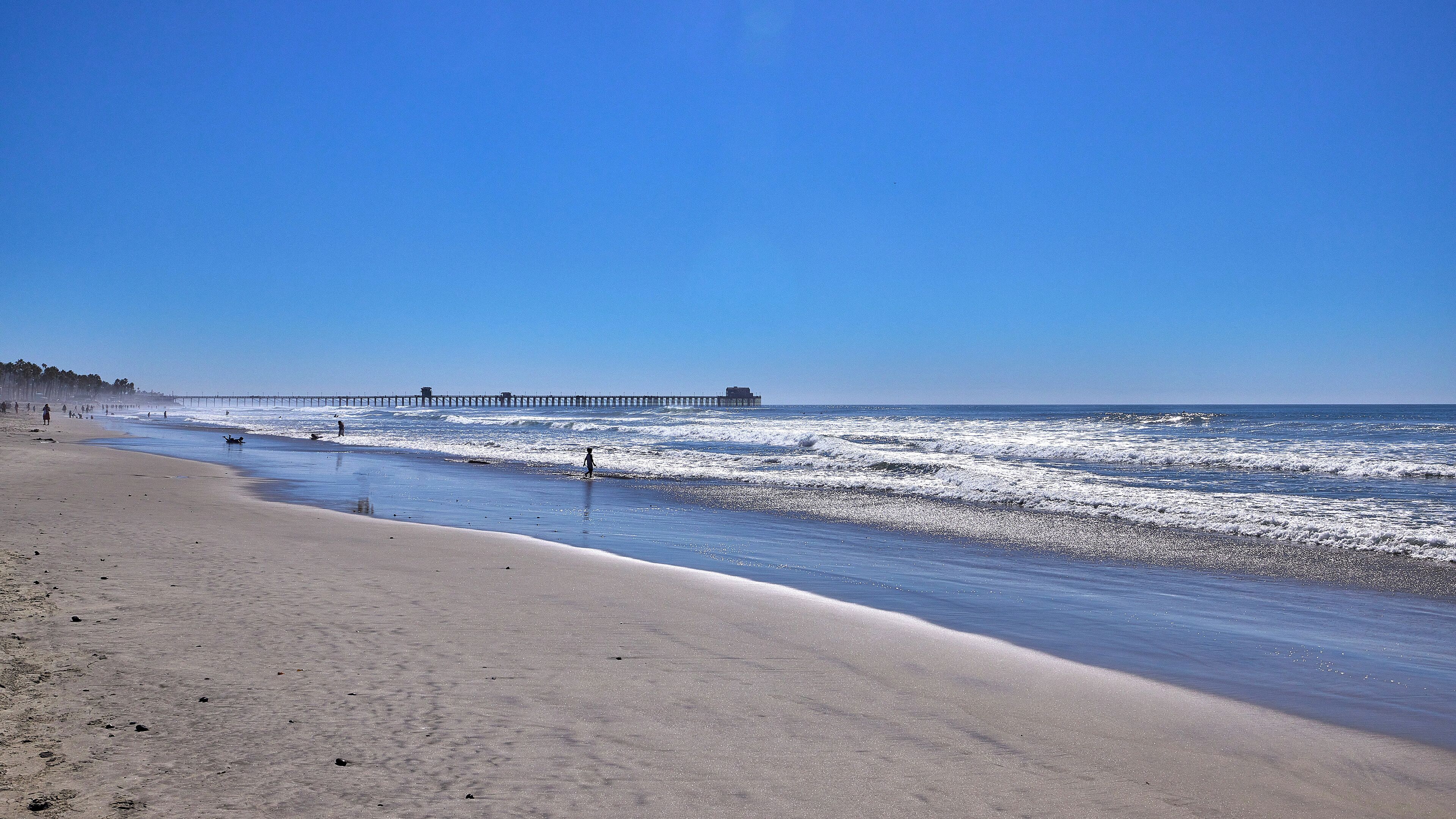 A beach with a pier extending into the ocean, sandy shore, and clear blue sky.