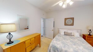 Una camera da letto con un letto, una cassettiera, uno specchio, una porta e una lampada a soffitto.