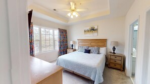 A bedroom with a bed, two bedside tables, a ceiling fan, a window with curtains, and a painting on the wall. - Ironwood 1231 (North Myrtle Beach)