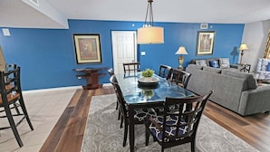 A dining area with a glass table, dark chairs, and a blue accent wall. - Yacht Club 2-704 (North Myrtle Beach)