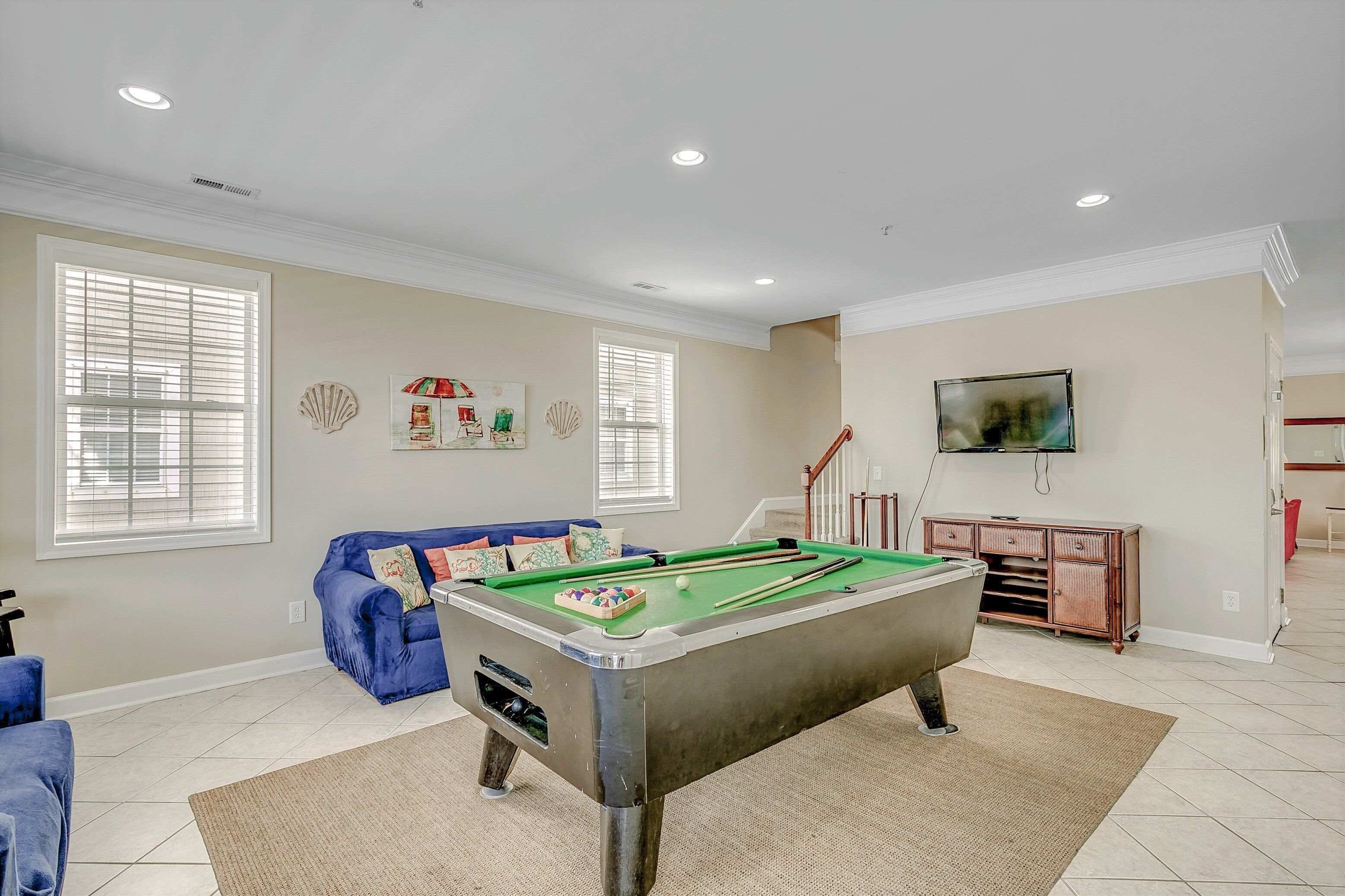 A spacious living room with a pool table, a blue sofa, and a television mounted on the wall.