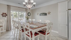 Comedor con mesa de madera, sillas blancas, una araña de techo, un reloj y una decoración de estrella de mar en la pared.
