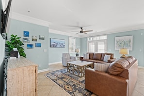 A living room with a brown leather sofa, a patterned rug, and a ceiling fan. - Grand Cayman Villas - I (North Myrtle Beach)